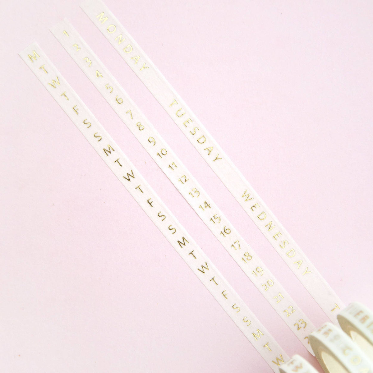 Three thin washi tape strips printed with day names and date numbers on pale background