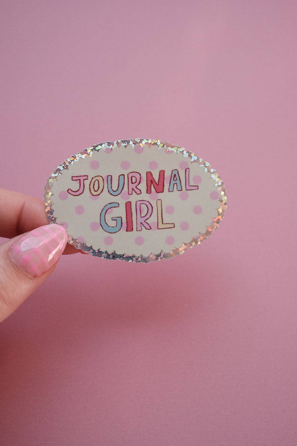 Single oval sticker reading “JOURNAL GIRL” with speckled border, held by a hand.