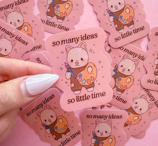 So Many Ideas vinyl sticker held by hand: pink cat with art palette and 'so many ideas' text