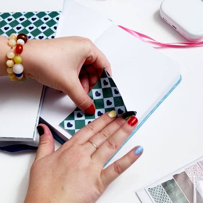 Hands placing black-and-green heart check stickers on a journal page