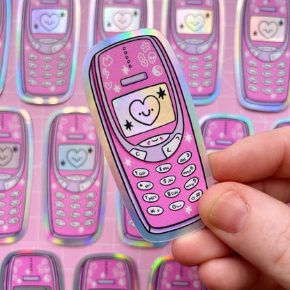 Pink holographic phone-shaped sticker with heart, smiley, stars, and button icons