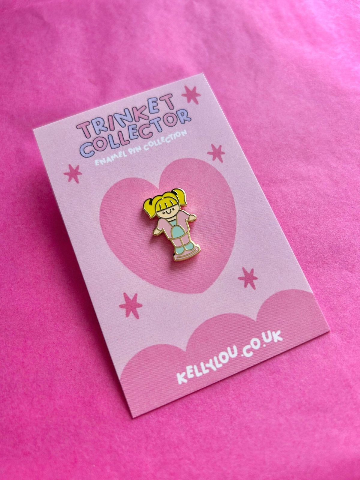 Mini enamel pin featuring a blonde doll character on a pink heart card backing