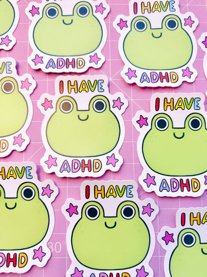Vinyl sticker sheet with repeating green frog faces, “I HAVE” and “ADHD” text, plus stars