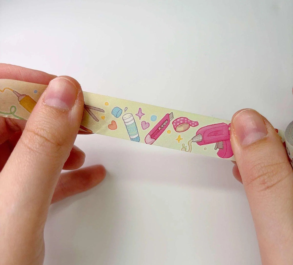 Washi tape strip with pastel doodle icons, held by hands