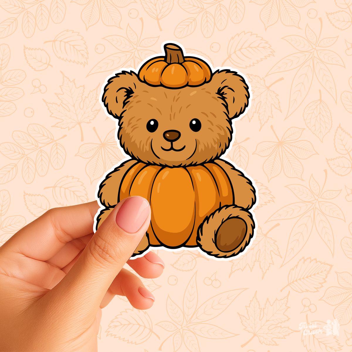 Hand holding a brown teddy bear sticker with an orange pumpkin