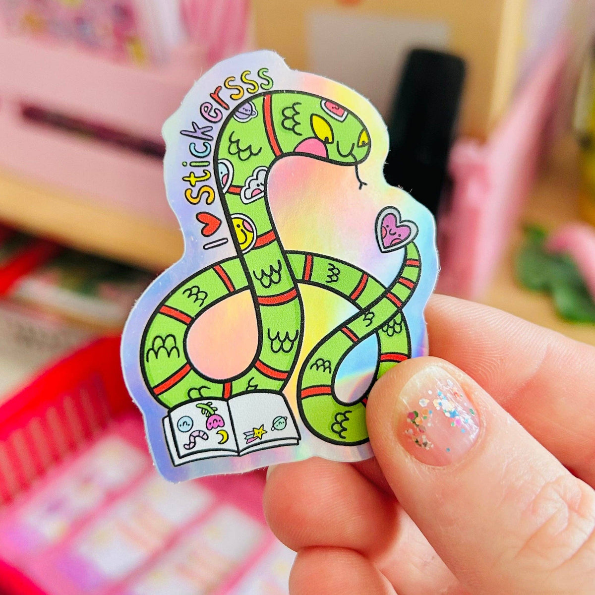 Rainbow holographic snake sticker, green serpent with hearts and text, held in hand