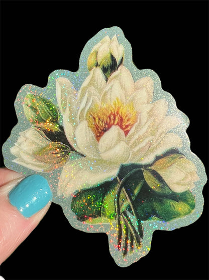 White lotus flower sticker, glitter-speckled petals and green leaves, held in fingertips