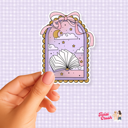 Book-shaped sticker with open-book illustration, stars, and bow; held by hand