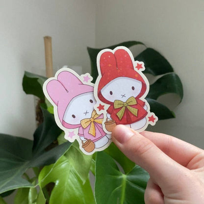 Handheld cartoon bunny sticker with red hood, bow, and small star details