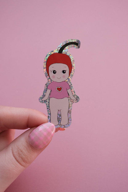 Baby cherry sticker held in hand, cartoon girl with patterned hood and pink heart shirt