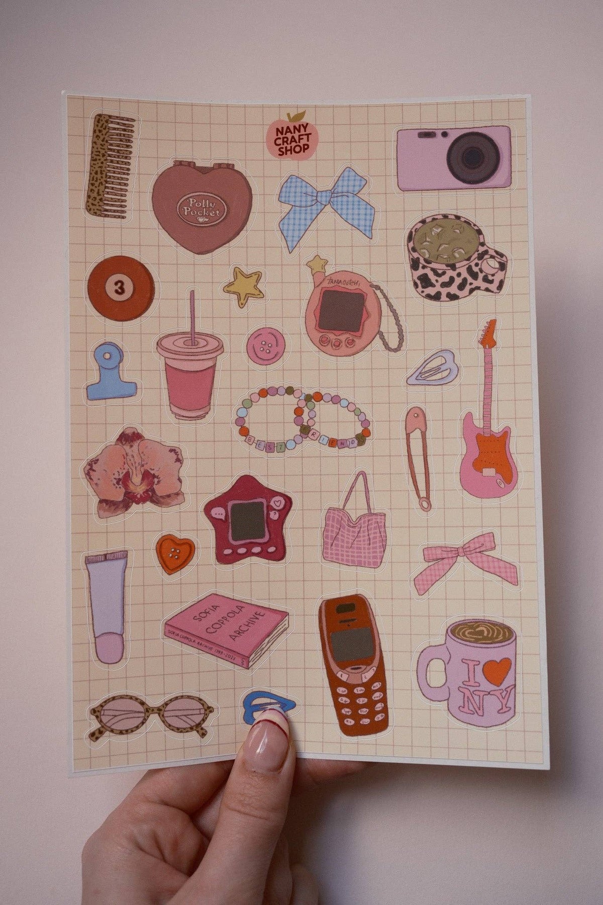 A5 sticker sheet held by hand, showing camera, hearts, phones, guitar and bracelets