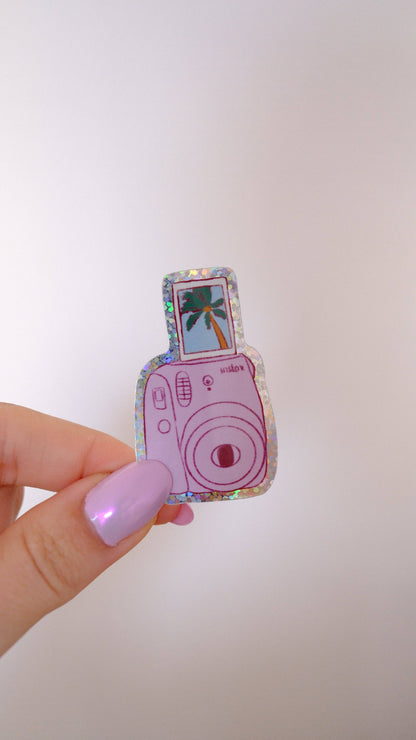 Pink polaroid camera sticker with palm tree photo, held between fingers