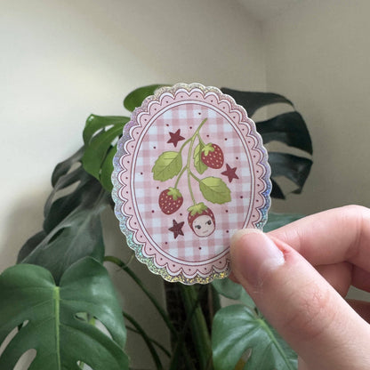 Strawberry medallion sticker held in hand, plaid center with berries and girl illustration