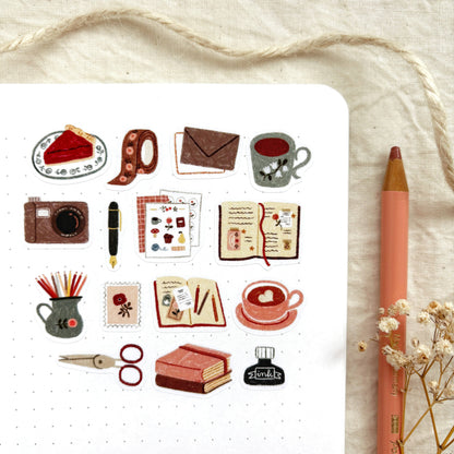 Sticker sheet close-up with teacup, camera, pencils, mug and notebook icons