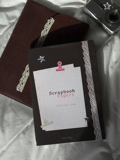 Scrapbook paper stack with dark brown cover, lace ribbon, star tag and pink binder clip