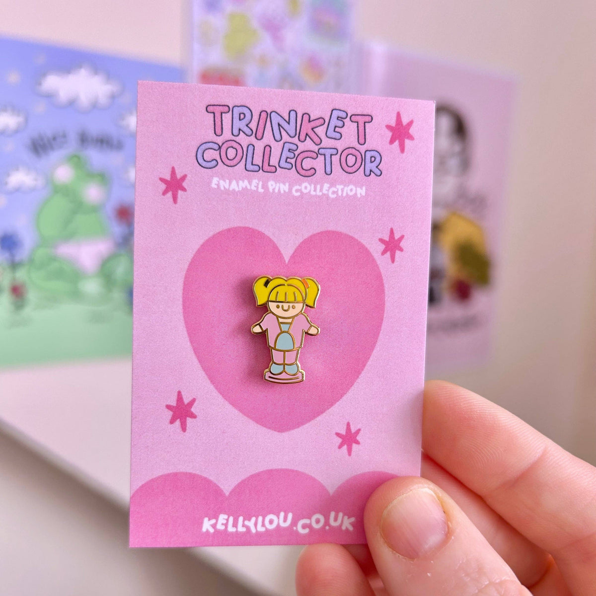 Mini enamel pin of blonde doll character on pink heart card with gold-tone details