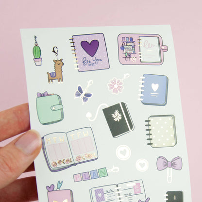 Planner sticker sheet held in hand with colorful notebook, butterfly, and floral icons