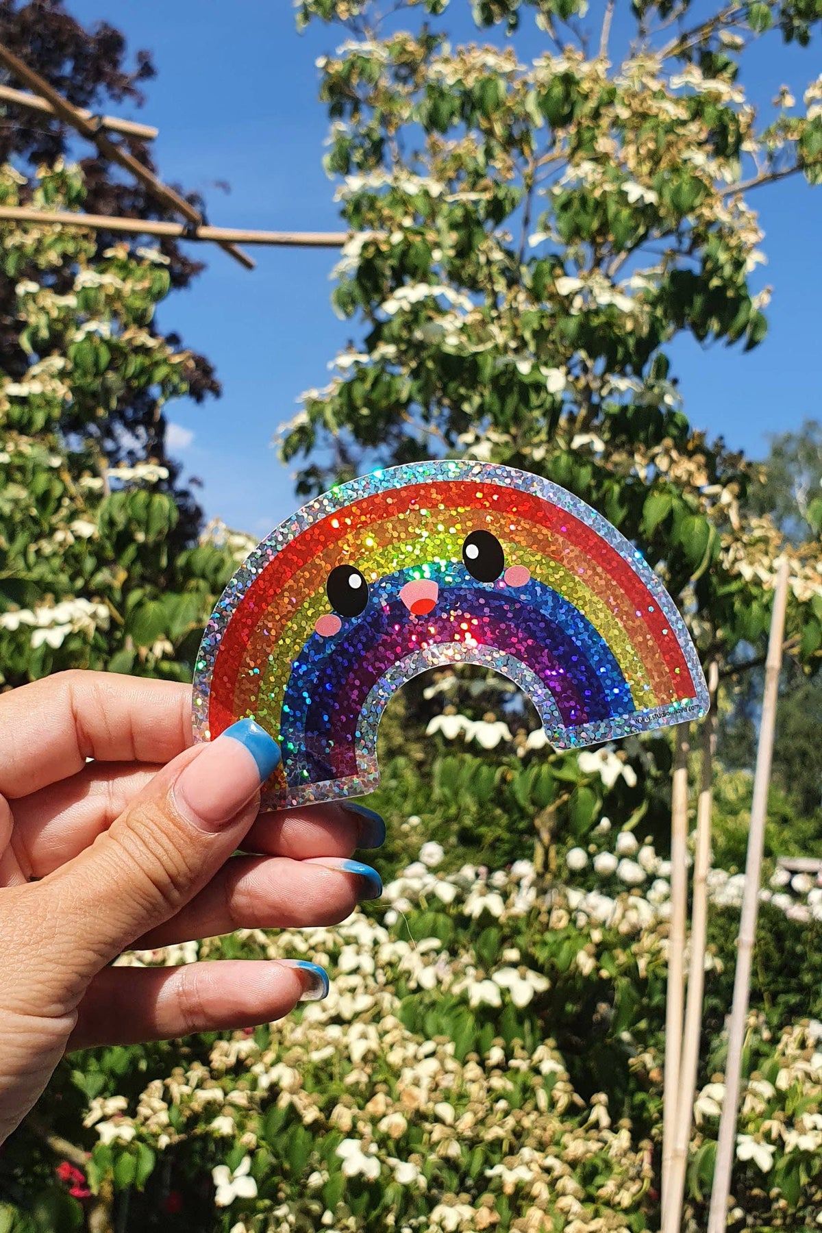 Hand holding rainbow glitter vinyl sticker with bear face and rainbow arc, sparkly glitter