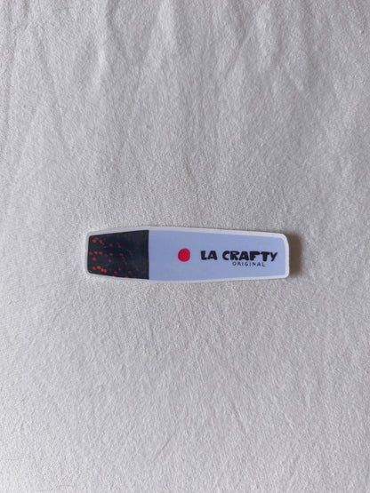 La crafty sticker on surface, white rounded label with black speckle end and red dot logo