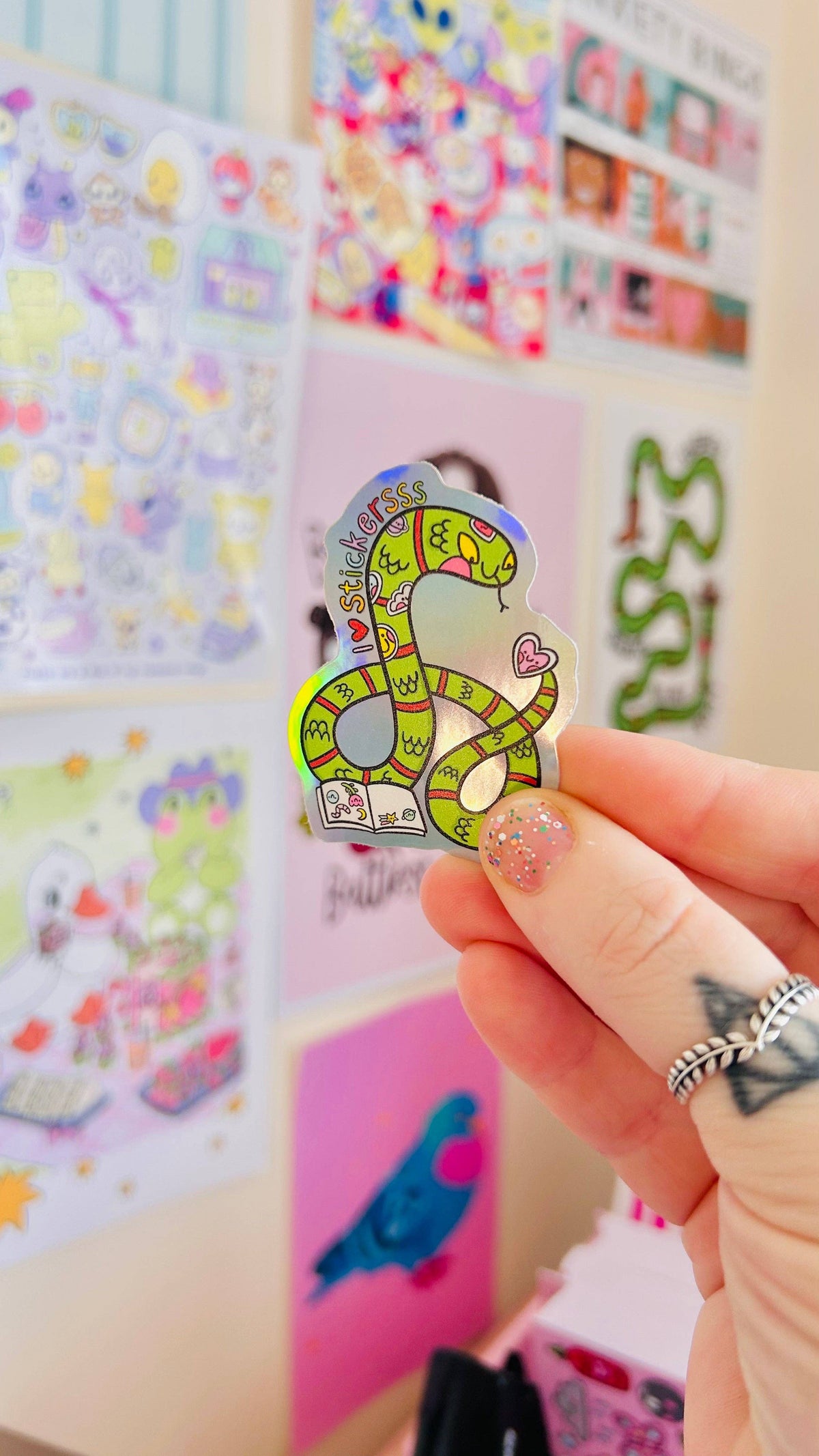 Rainbow holographic snake sticker, green curled serpent with hearts, held near other stickers