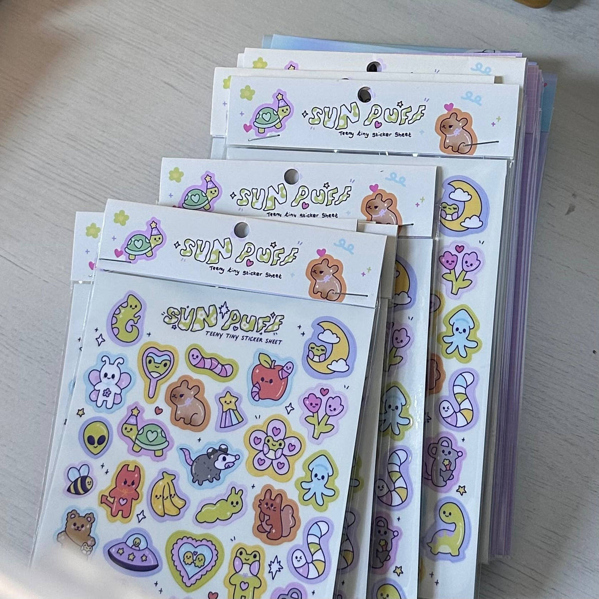 Stacked sticker sheets with SUN PUFF characters, hearts, stars, and small icons