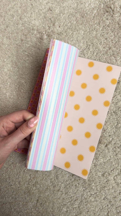 Open scrapbook paper, pink-blue stripes on left and yellow sun icons on right