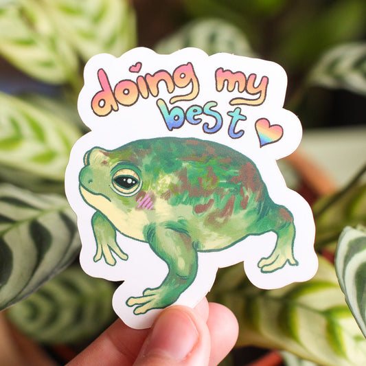 Vinyl sticker held in hand with 'Doing my best' text and green frog illustration.