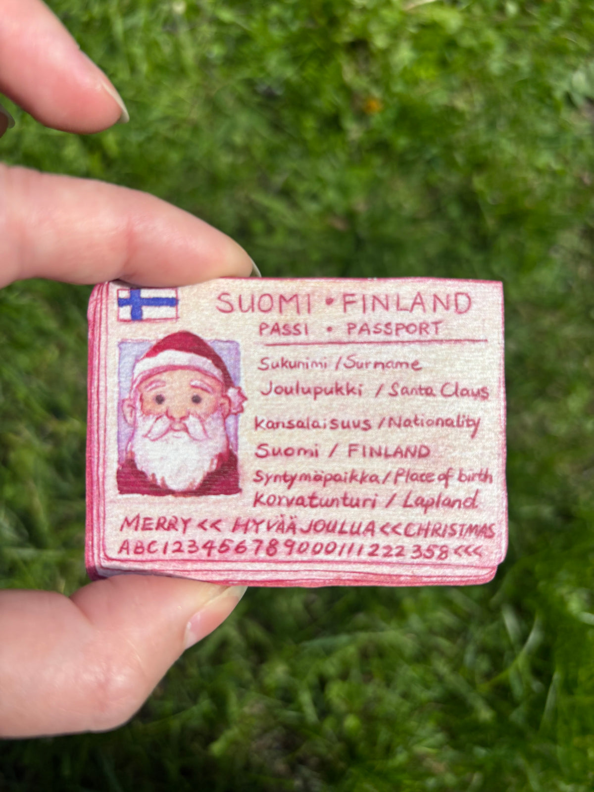Wooden Santa passport magnet with red text and Finnish flag icon on rectangular tag