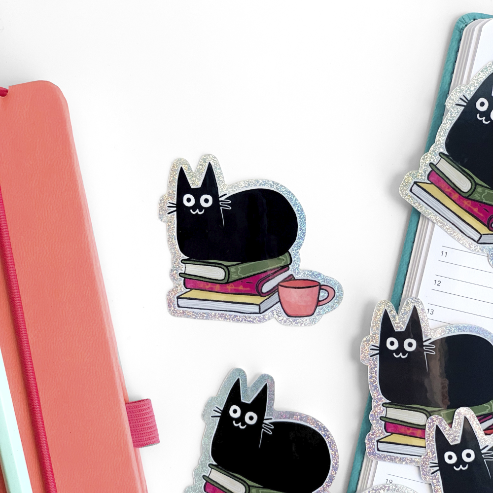 Vinyl stickers showing black cat with colorful stacked books and a pink mug